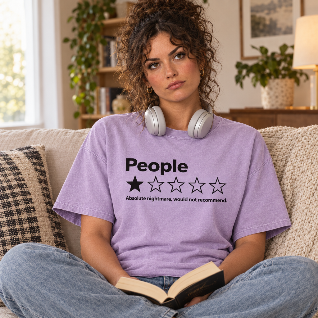 Woman wearing Orchid Comfort Colors People One Star Review shirt on the couch with headphones and a book