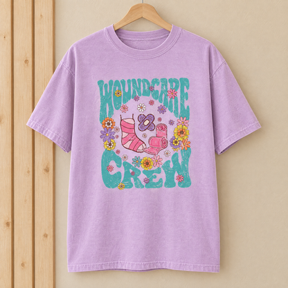 Wound Care Crew Comfort Colors shirt in Orchid on a wooden hanger