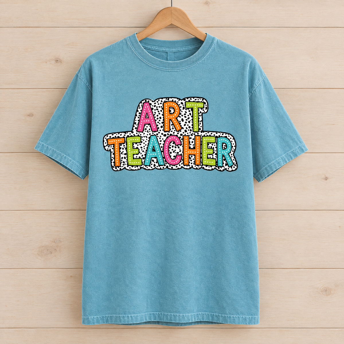 Art Teacher Comfort Colors shirt in Lagoon Blue on a wooden hanger