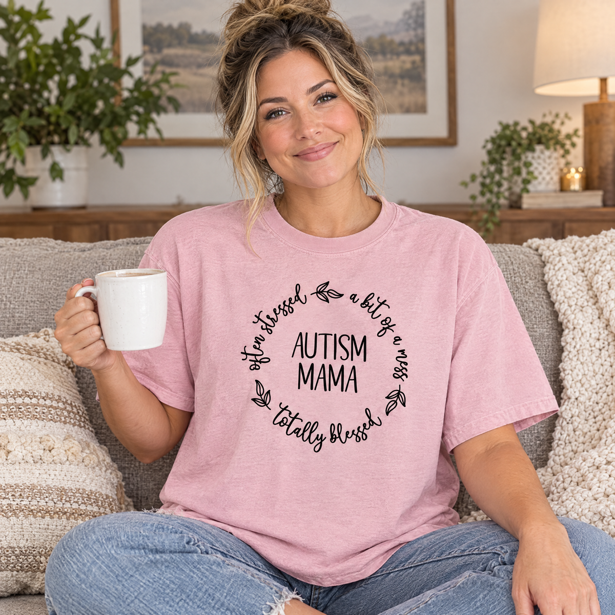 Mom wearing a Blossom pink Comfort Colors Autism Mama shirt on a cozy couch with coffee