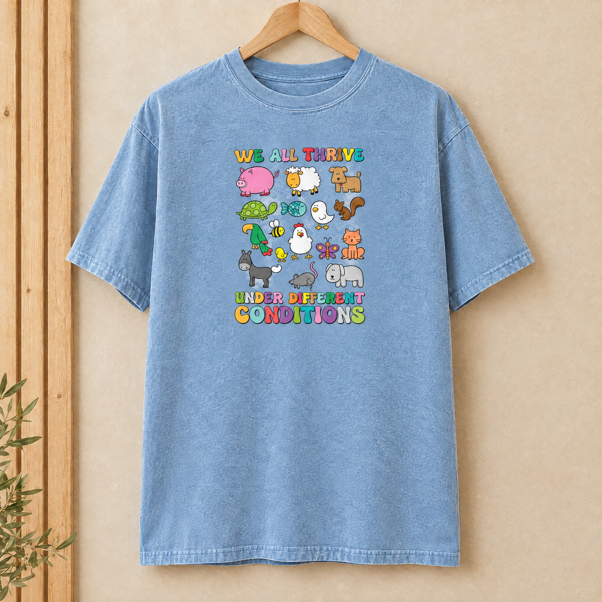 We All Thrive Under Different Conditions Comfort Colors shirt in Chambray on a wooden hanger