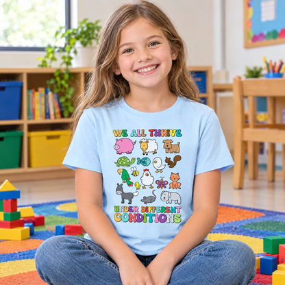 Girl wearing a light blue youth We All Thrive Under Different Conditions tee on a classroom rug