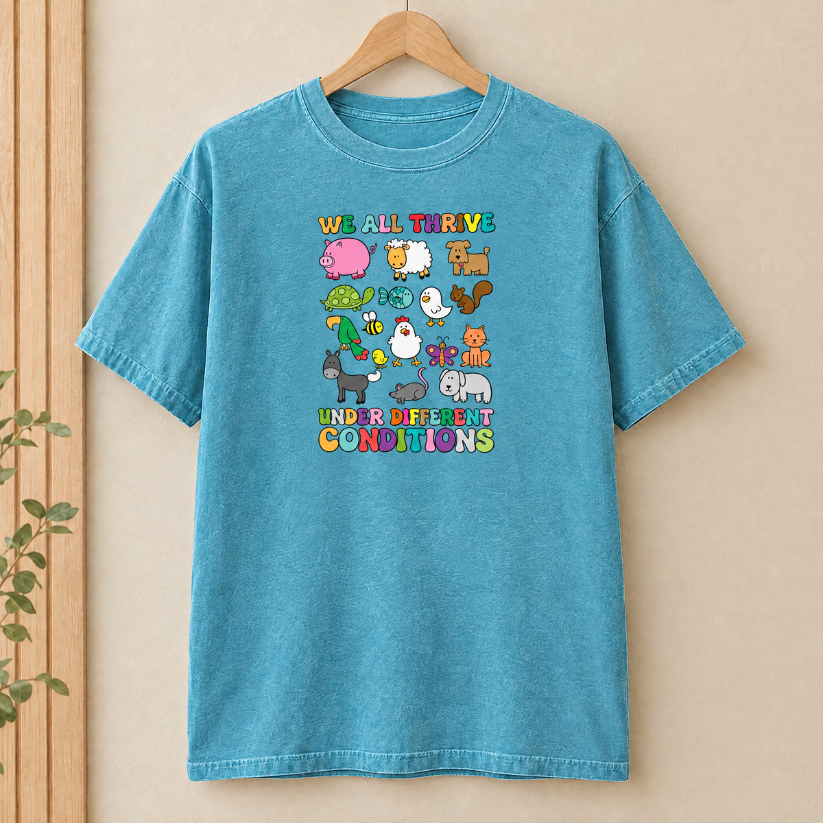 We All Thrive Under Different Conditions Comfort Colors shirt in Lagoon Blue on a wooden hanger