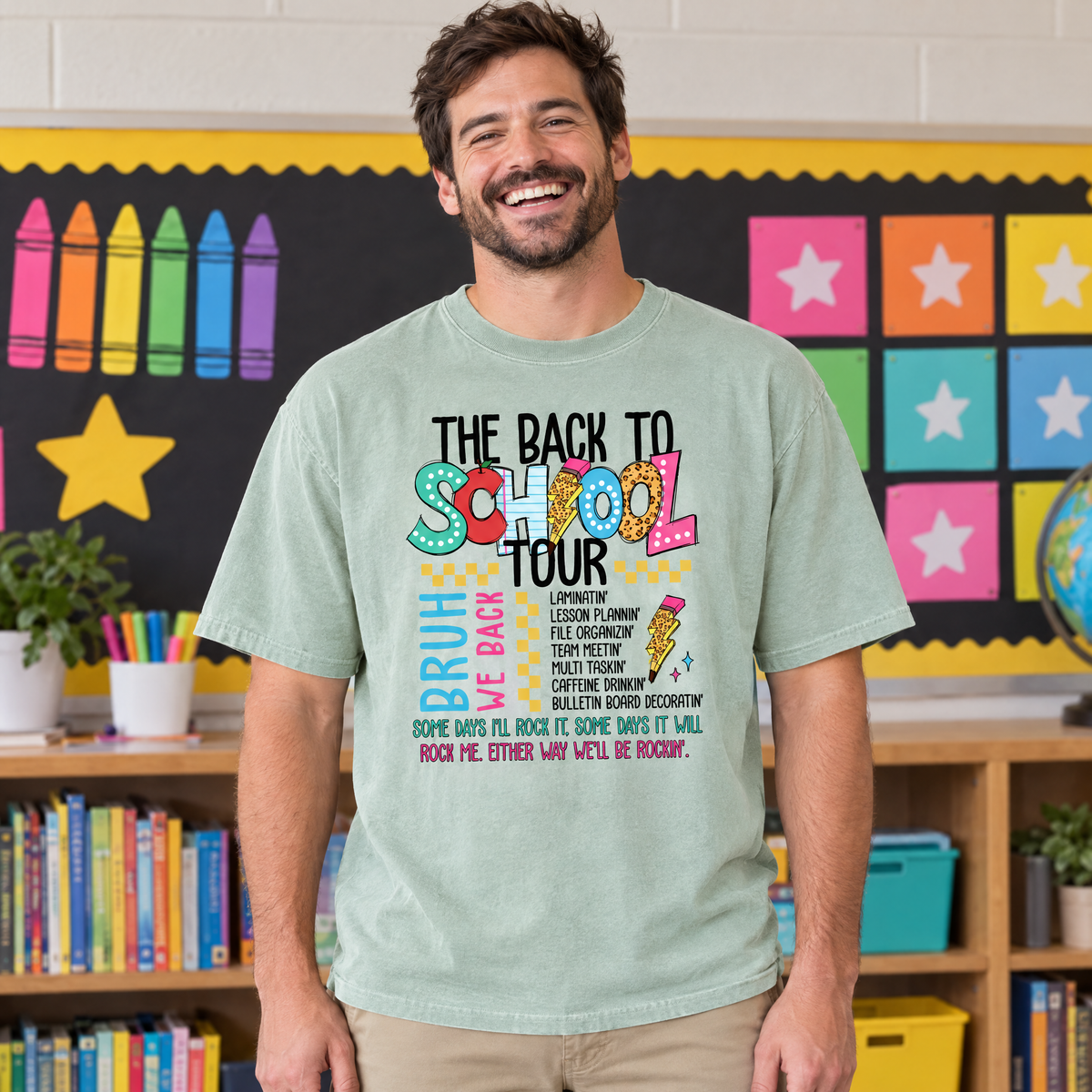 Male teacher wearing a Light Green Comfort Colors Back to School Tour shirt in front of a colorful classroom bulletin board