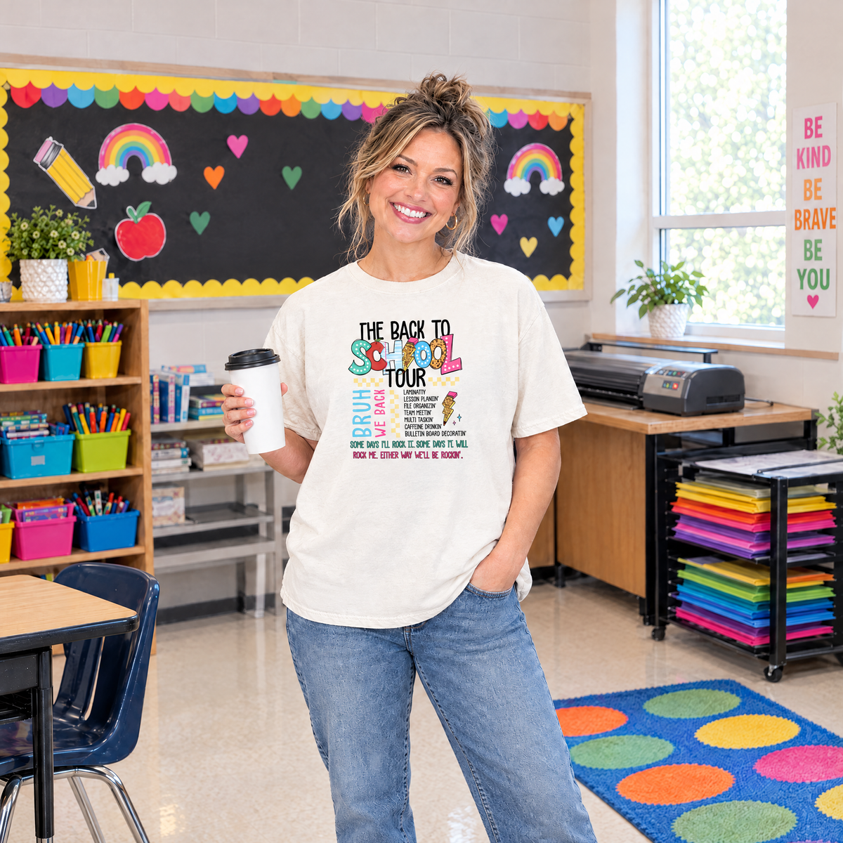 Teacher wearing an Ivory Comfort Colors Back to School Tour shirt holding coffee in a colorful classroom
