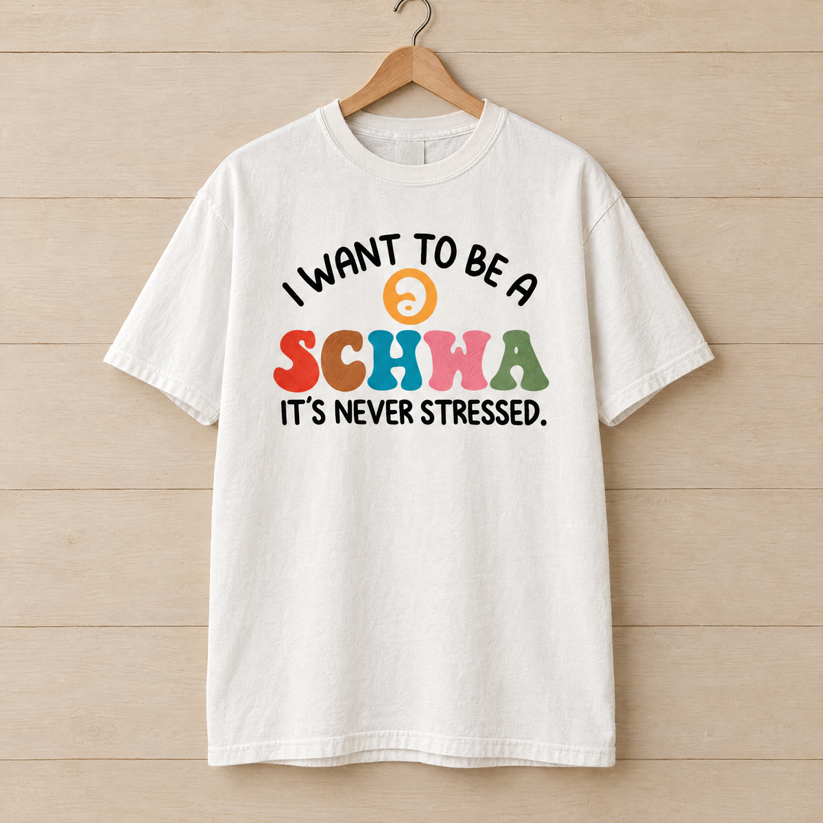 I Want To Be A Schwa shirt in White Comfort Colors, on a wooden hanger