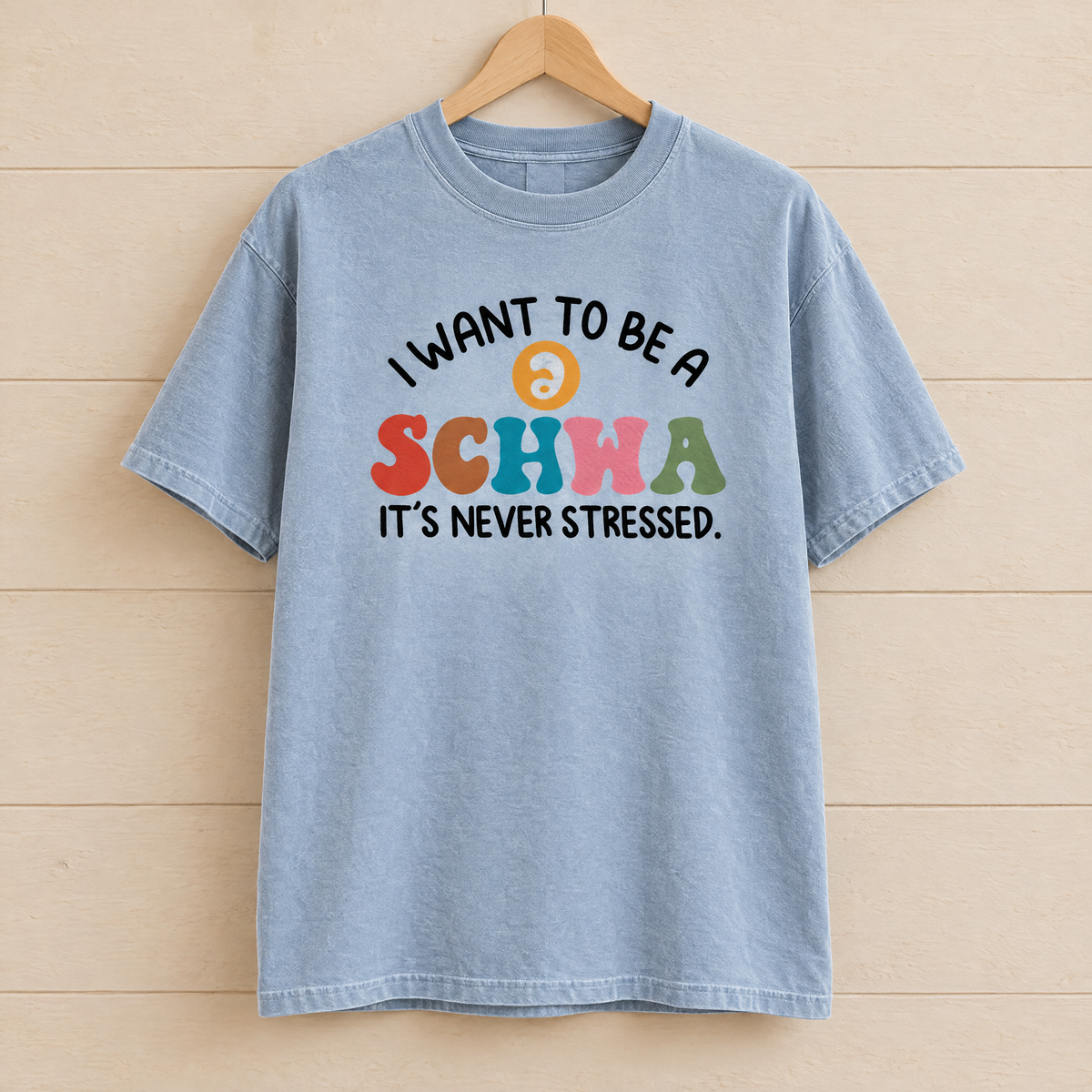 I Want To Be A Schwa shirt in Chambray Comfort Colors, on a wooden hanger