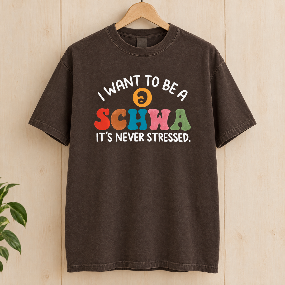 I Want To Be A Schwa shirt in Espresso Comfort Colors, on a wooden hanger