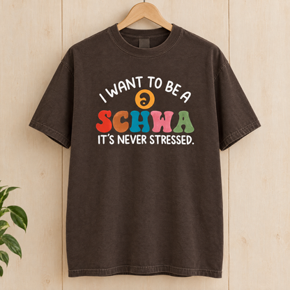 I Want To Be A Schwa shirt in Espresso Comfort Colors, on a wooden hanger