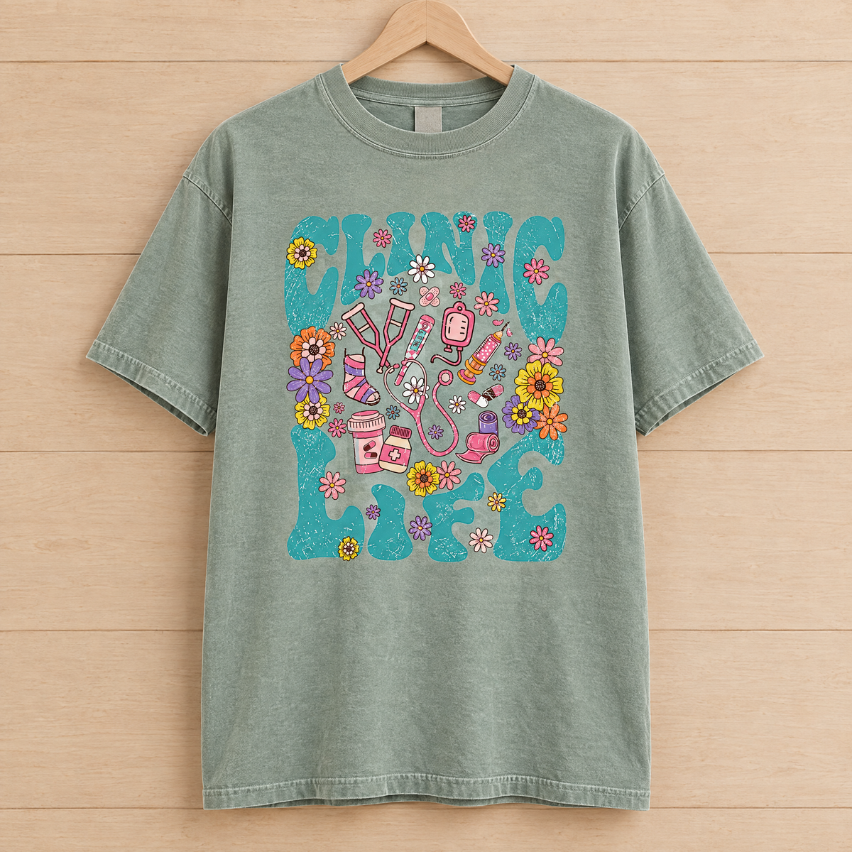 Clinic Life shirt in Sage Comfort Colors, on a wooden hanger