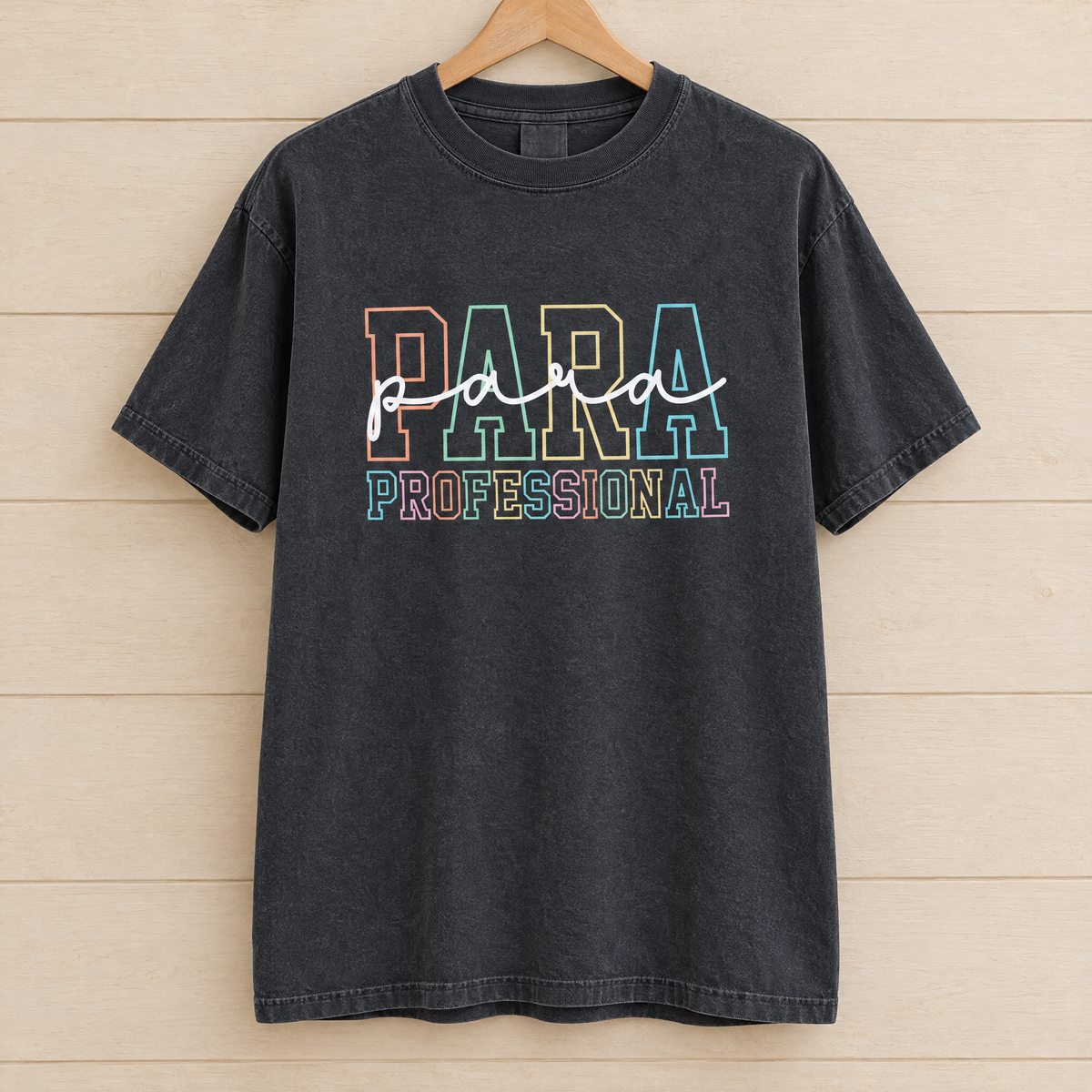 Paraprofessional shirt in Black Comfort Colors, on a wooden hanger