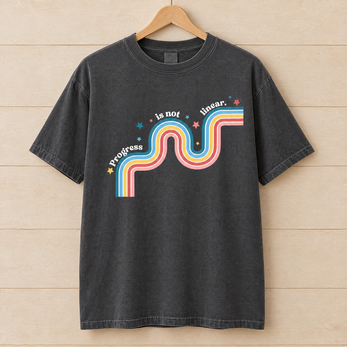 Progress Is Not Linear shirt in Pepper Comfort Colors, on a wooden hanger