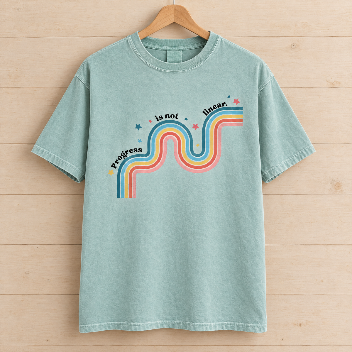 Progress Is Not Linear shirt in Seafoam Comfort Colors, on a wooden hanger