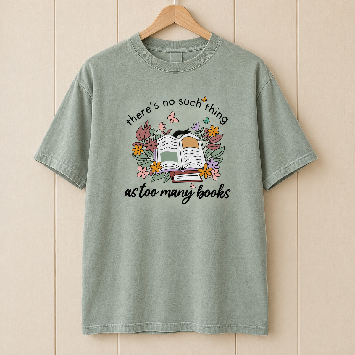 Too Many Books shirt in Sage Comfort Colors, on a wooden hanger