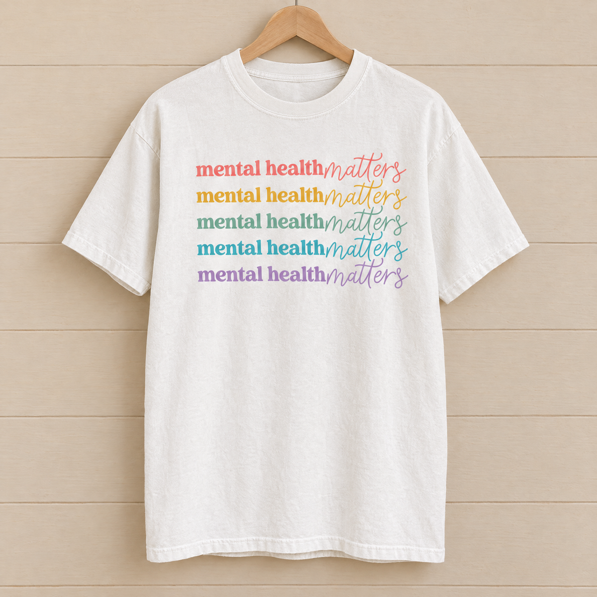 Mental Health Matters rainbow shirt in White Comfort Colors on a wooden hanger