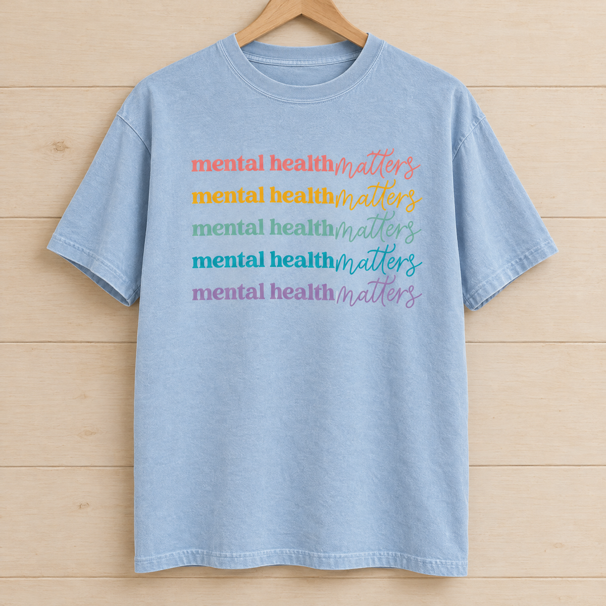 Mental Health Matters rainbow shirt in Chambray Comfort Colors on a wooden hanger