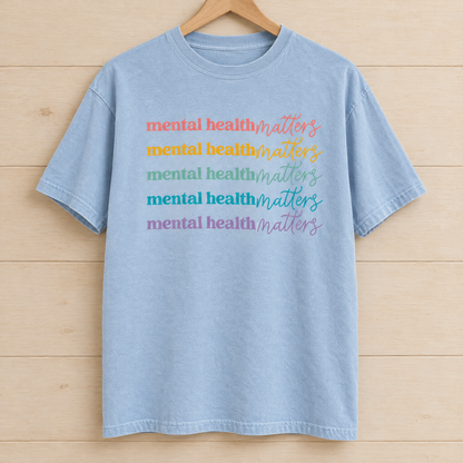 Mental Health Matters rainbow shirt in Chambray Comfort Colors on a wooden hanger