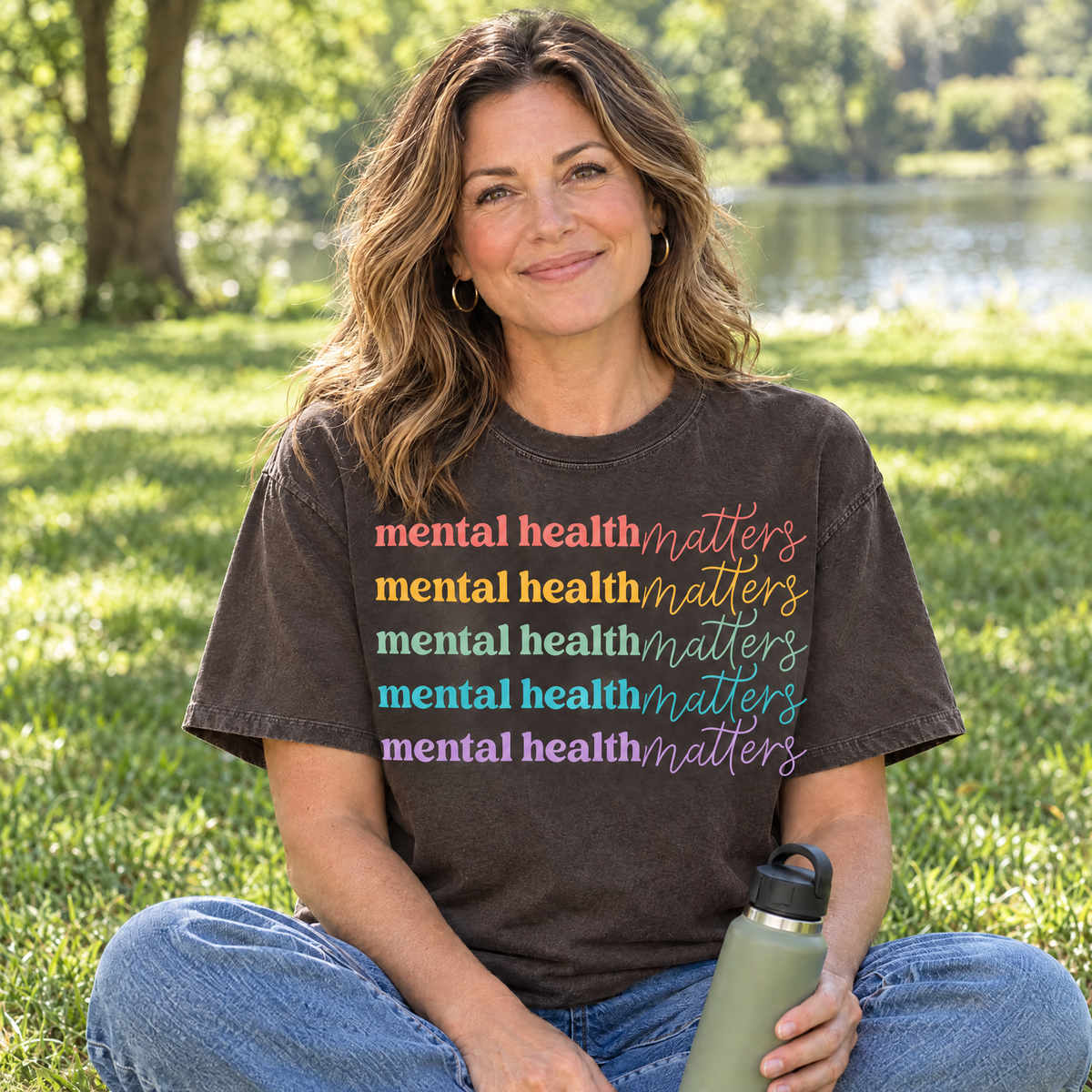 Mental Health Matters rainbow shirt in Espresso Comfort Colors, woman sitting on the grass in a park
