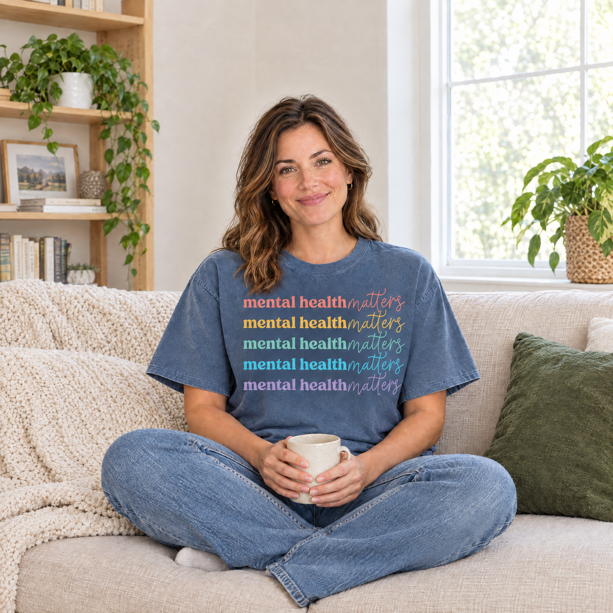 Mental Health Matters rainbow shirt in Blue Jean Comfort Colors, woman sitting on a cozy sofa with a mug