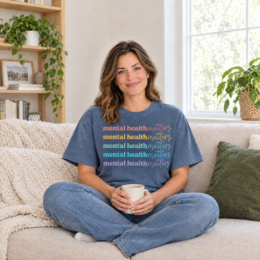 Mental Health Matters rainbow shirt in Blue Jean Comfort Colors, woman sitting on a cozy sofa with a mug