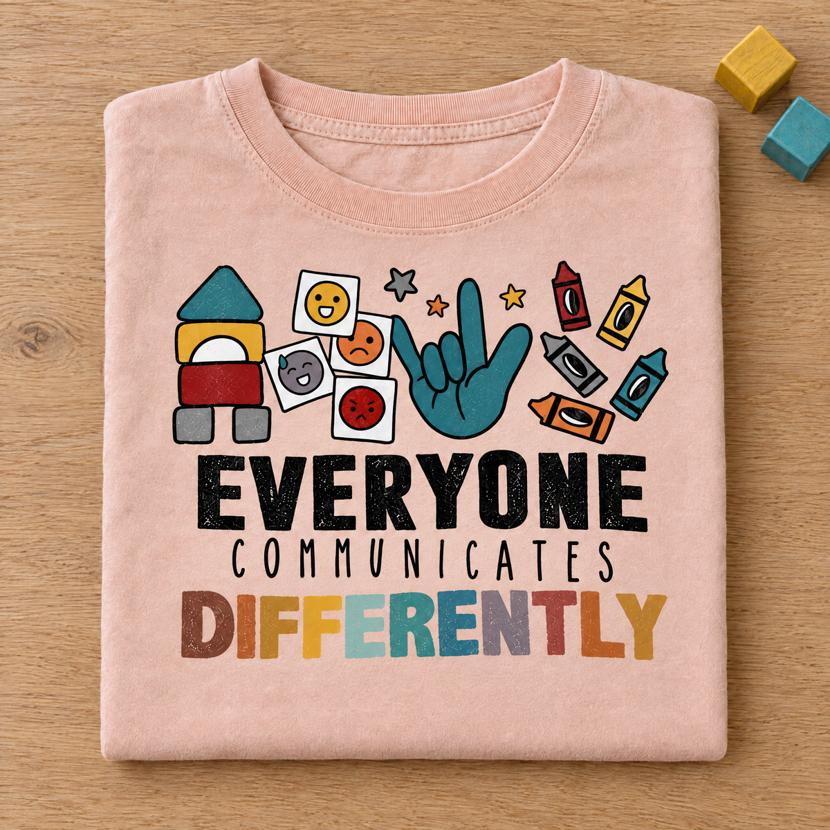 Everyone Communicates Differently autism acceptance shirt in Peachy Comfort Colors neatly folded