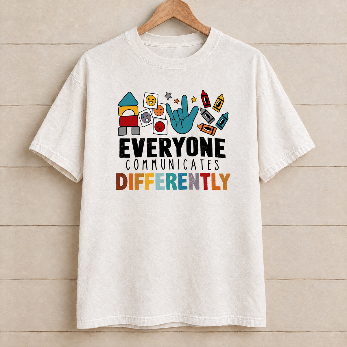 Everyone Communicates Differently autism acceptance shirt in White Comfort Colors on a wooden hanger