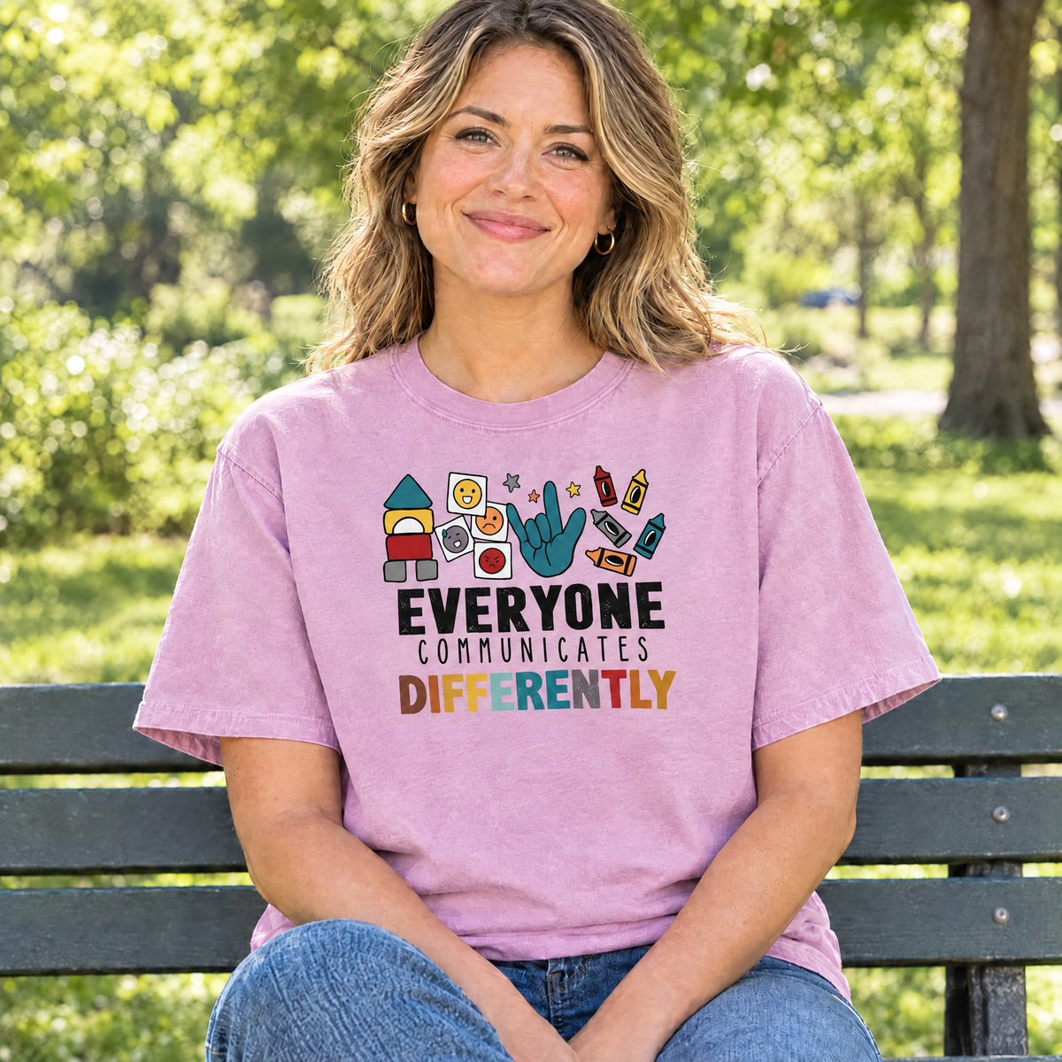 Everyone Communicates Differently autism acceptance shirt in Orchid Comfort Colors, mom sitting on a park bench