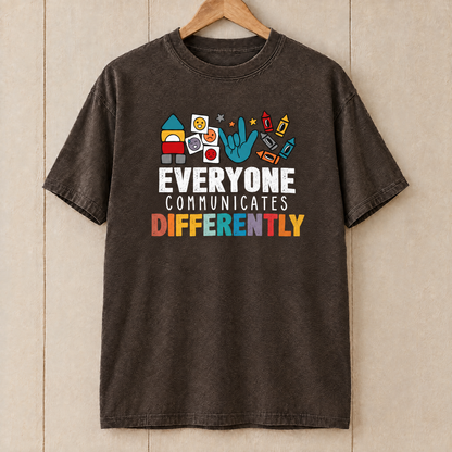 Everyone Communicates Differently autism acceptance shirt in Espresso Comfort Colors on a wooden hanger