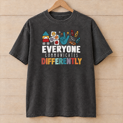 Everyone Communicates Differently autism acceptance shirt in Pepper Comfort Colors on a wooden hanger