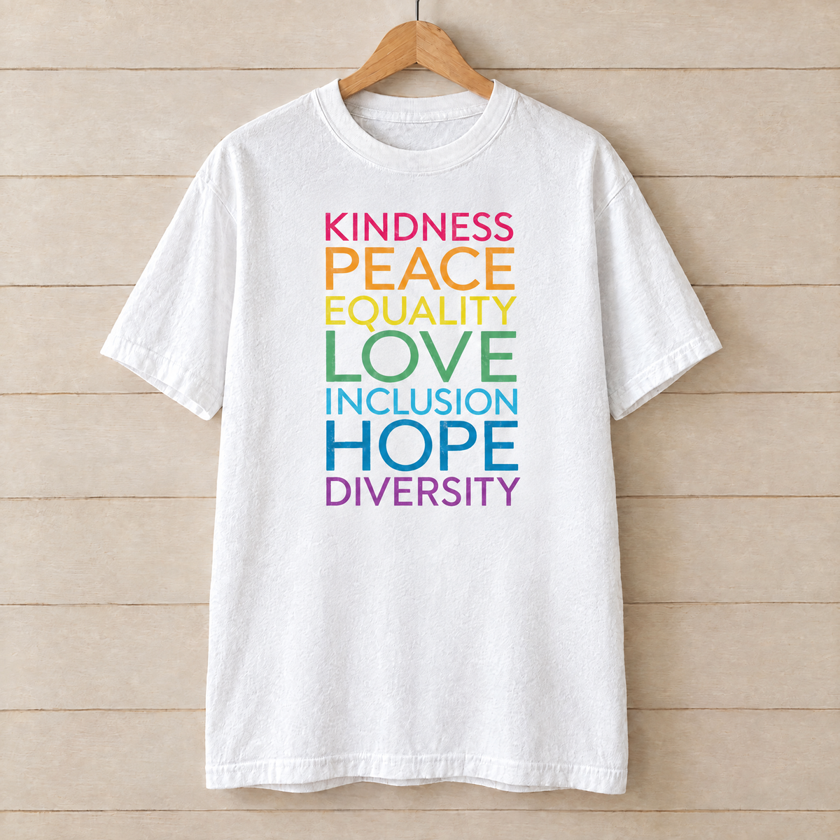 Kindness Peace Equality Love rainbow words shirt in White Comfort Colors on a wooden hanger