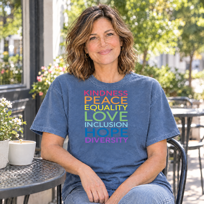 Kindness Peace Equality Love rainbow words shirt in Blue Jean Comfort Colors, woman sitting at an outdoor cafe table