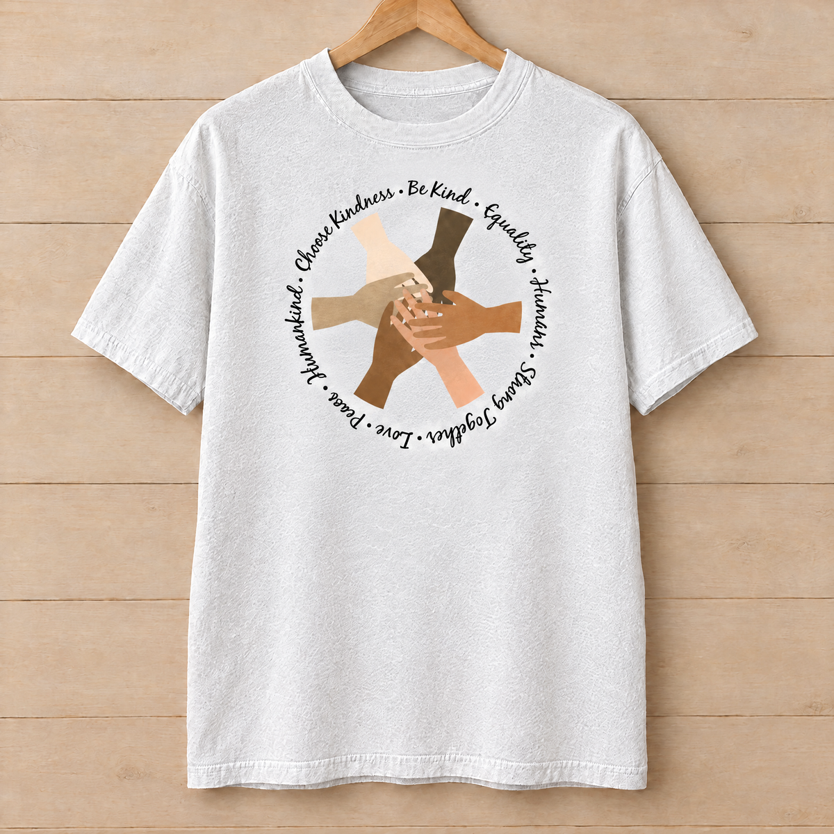 Choose Kindness diverse hands circle shirt in White Comfort Colors on a wooden hanger