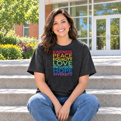 Kindness Peace Equality Love rainbow words shirt in Black Comfort Colors, woman sitting on community center steps