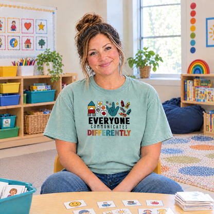 Everyone Communicates Differently autism acceptance shirt in Seafoam Comfort Colors, special education teacher sitting at a classroom table with picture cards