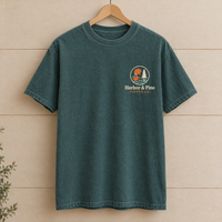 Custom company logo pocket print shirt in Blue Spruce Comfort Colors with a colorful coffee shop logo on a wooden hanger