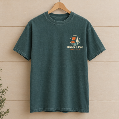 Custom company logo pocket print shirt in Blue Spruce Comfort Colors with a colorful coffee shop logo on a wooden hanger