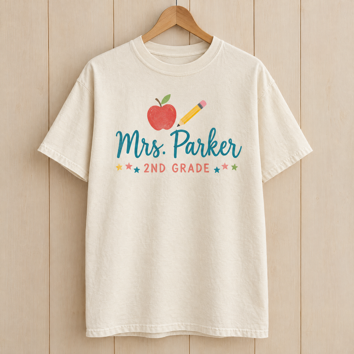 Custom teacher name shirt in Natural Ivory Comfort Colors with an apple, pencil and Mrs. Parker 2nd Grade on a hanger