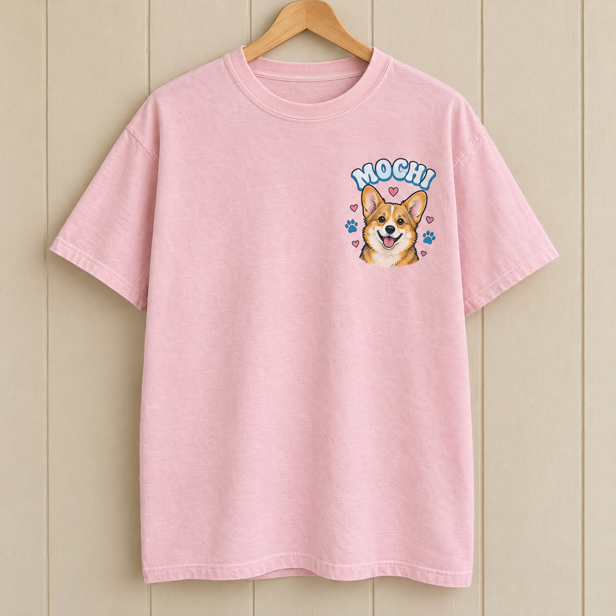 Pocket pet portrait shirt in Blossom pink Comfort Colors with a small cartoon corgi named Mochi on a hanger