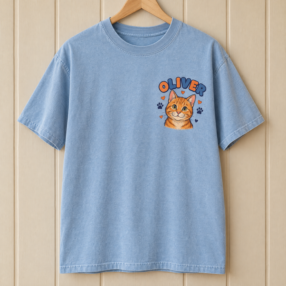 Pocket cat portrait shirt in Chambray Comfort Colors with a small cartoon orange tabby named Oliver on a hanger