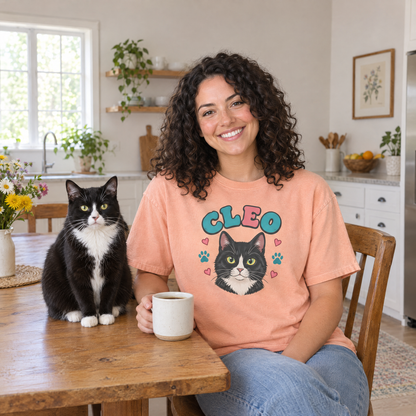 Cat mom at her kitchen table with her tuxedo cat, wearing a Peachy Comfort Colors shirt with a cartoon portrait of Cleo