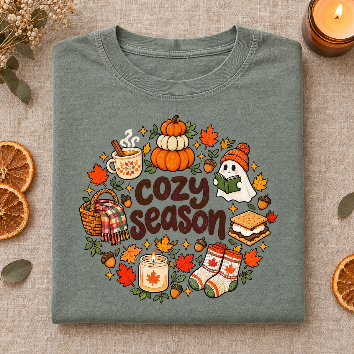 Cute autumn Cozy Season tee in Sage, folded with dried orange slices and a candle