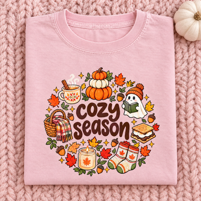 Cute fall Cozy Season tee in Blossom pink, folded on a knit blanket with a white pumpkin