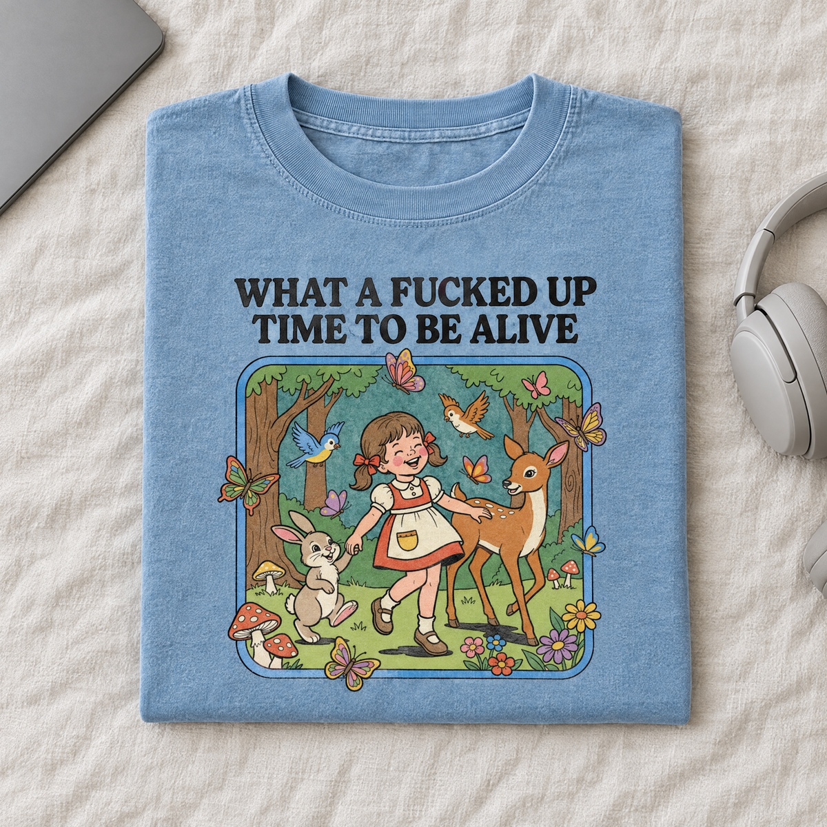 Sarcastic vintage cartoon tee in Chambray, folded with headphones and a laptop