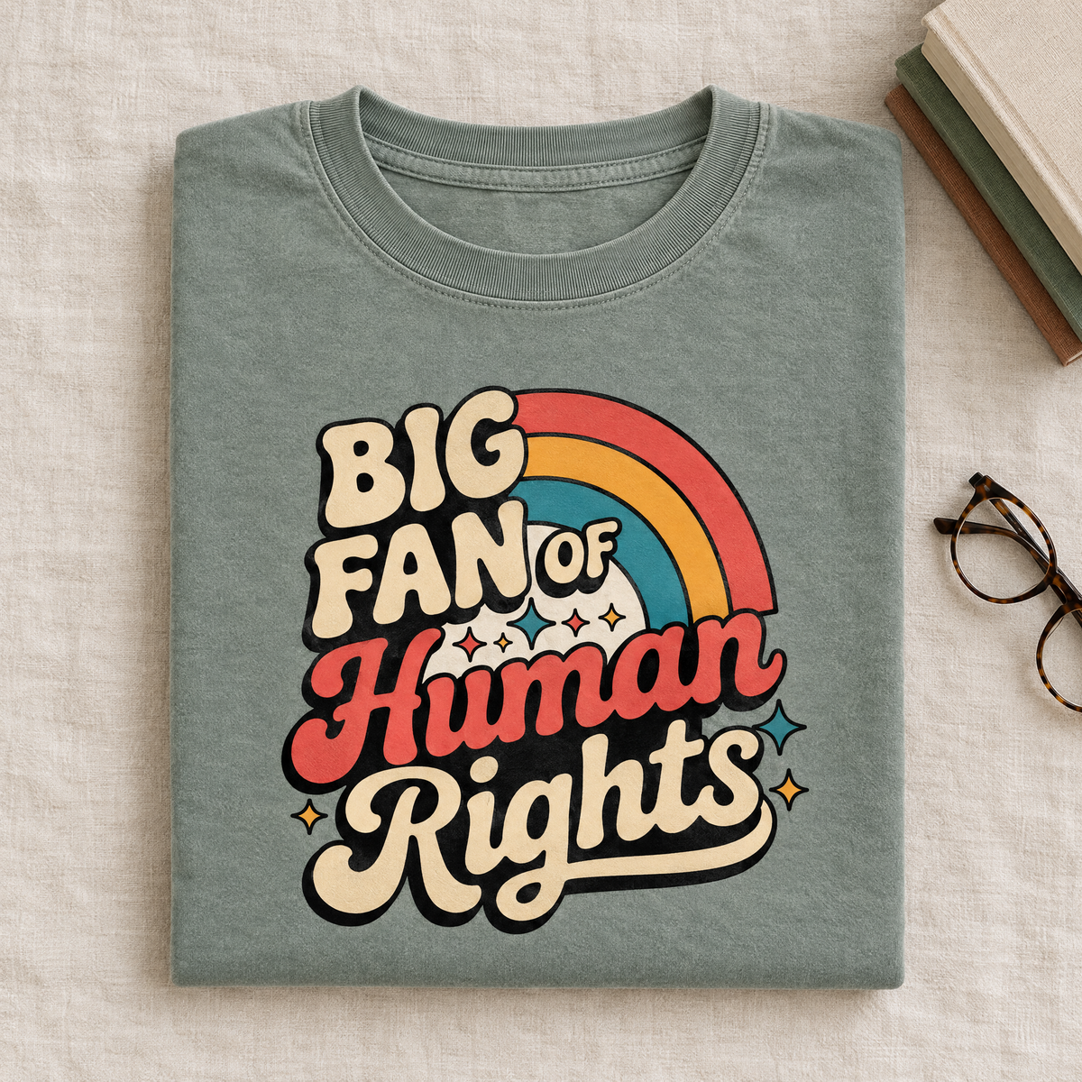 Social justice rainbow tee in Sage, folded with books and glasses