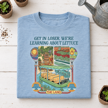 Chambray light blue Learning About Lettuce shirt folded next to a vintage watering can