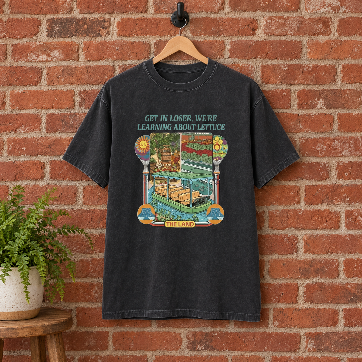 Black Learning About Lettuce shirt on a hanger against a red brick wall