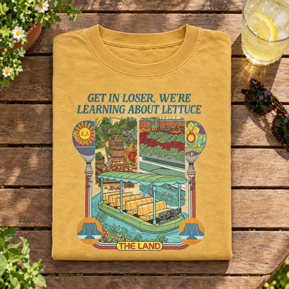 Mustard Learning About Lettuce shirt folded on a garden table with iced lemonade
