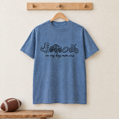 Blue Jean In My Boy Mom Era shirt hanging on a wooden peg rail with a football below