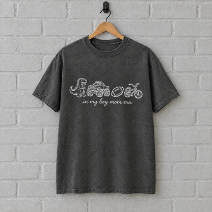 Pepper grey boy mom shirt with white print on a hanger against a painted brick wall