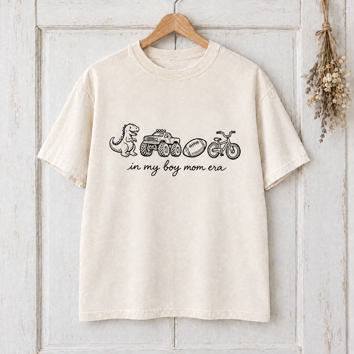 Ivory boy mom era shirt on a hanger on a whitewashed door